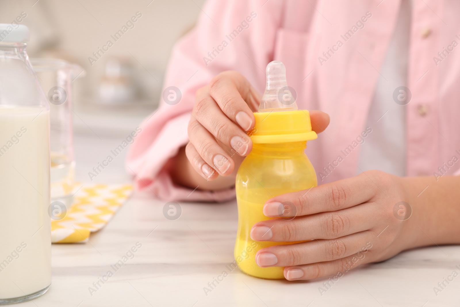 Photo of Woman preparing infant formula at table indoors, closeup. Baby milk