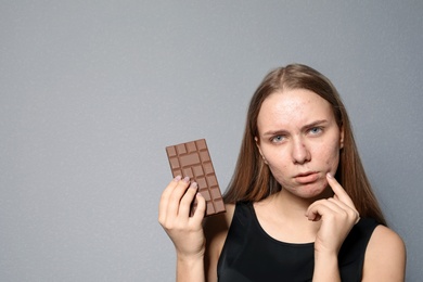 Young woman with acne problem holding chocolate bar on color background. Skin allergy