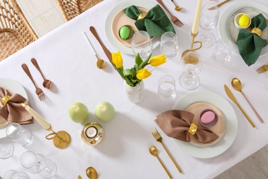 Festive Easter table setting with painted eggs, burning candles and yellow tulips, flat lay