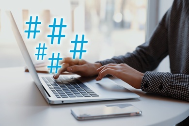 Image of Woman using modern laptop at table, closeup. Hashtag symbols over device