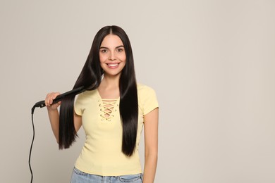 Photo of Beautiful happy woman using hair iron on light grey background. Space for text