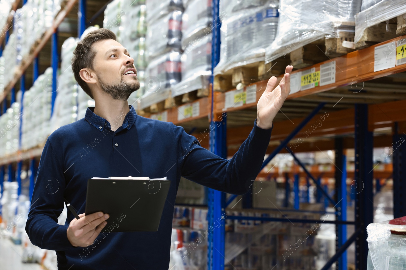 Photo of Happy manager holding clipboard in warehouse with lots of products