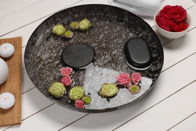 Photo of Plate with water, flowers and stones on white wooden floor. Pedicure procedure