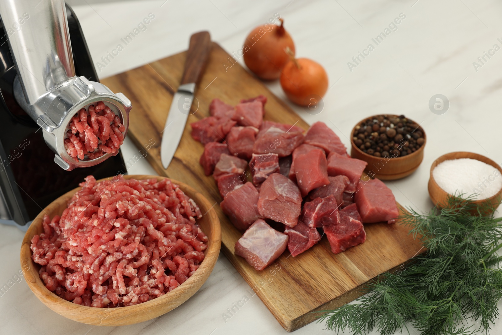 Photo of Electric meat grinder with beef and products on white marble table, above view