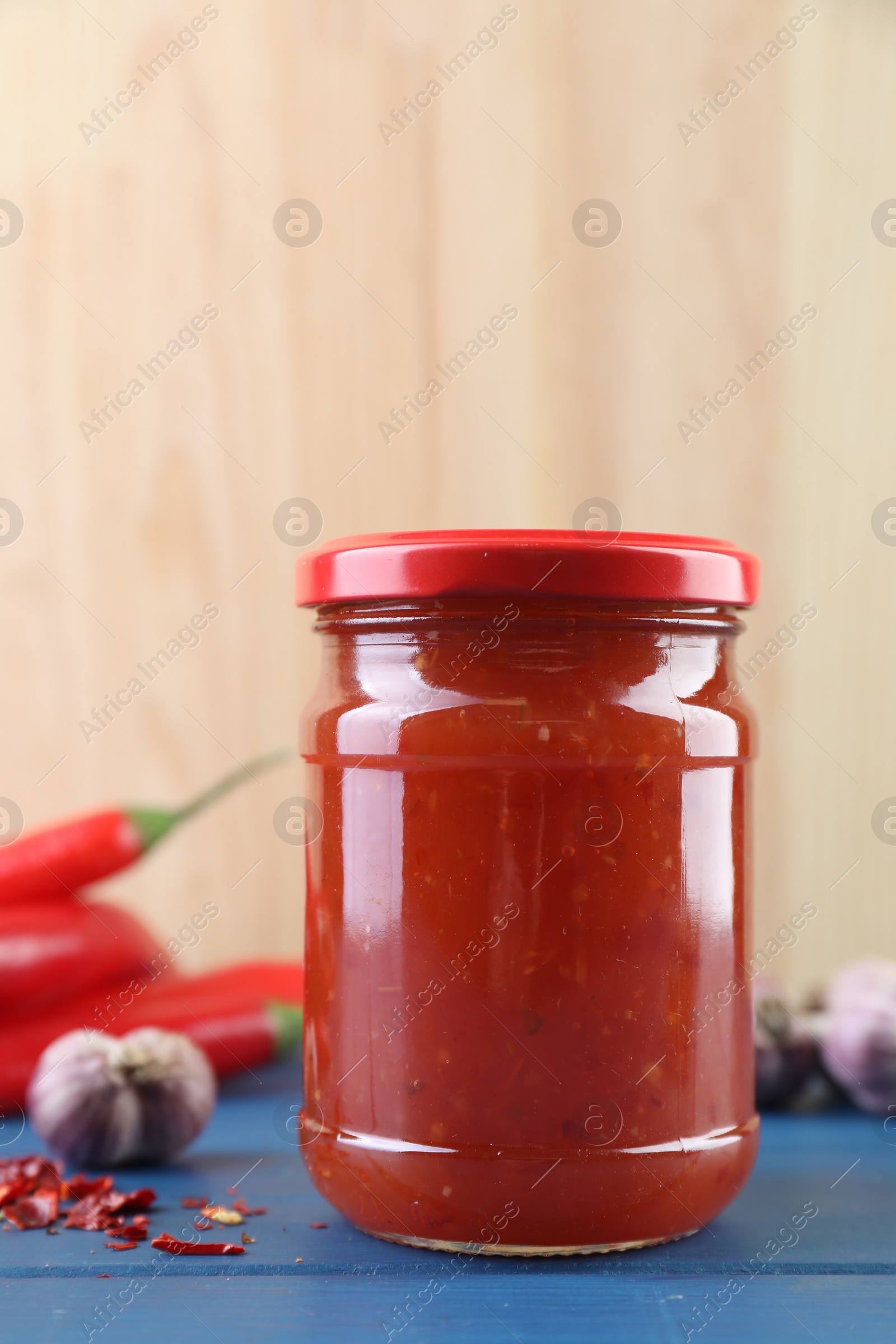 Photo of Spicy chili sauce in jar, garlic and peppers on blue wooden table