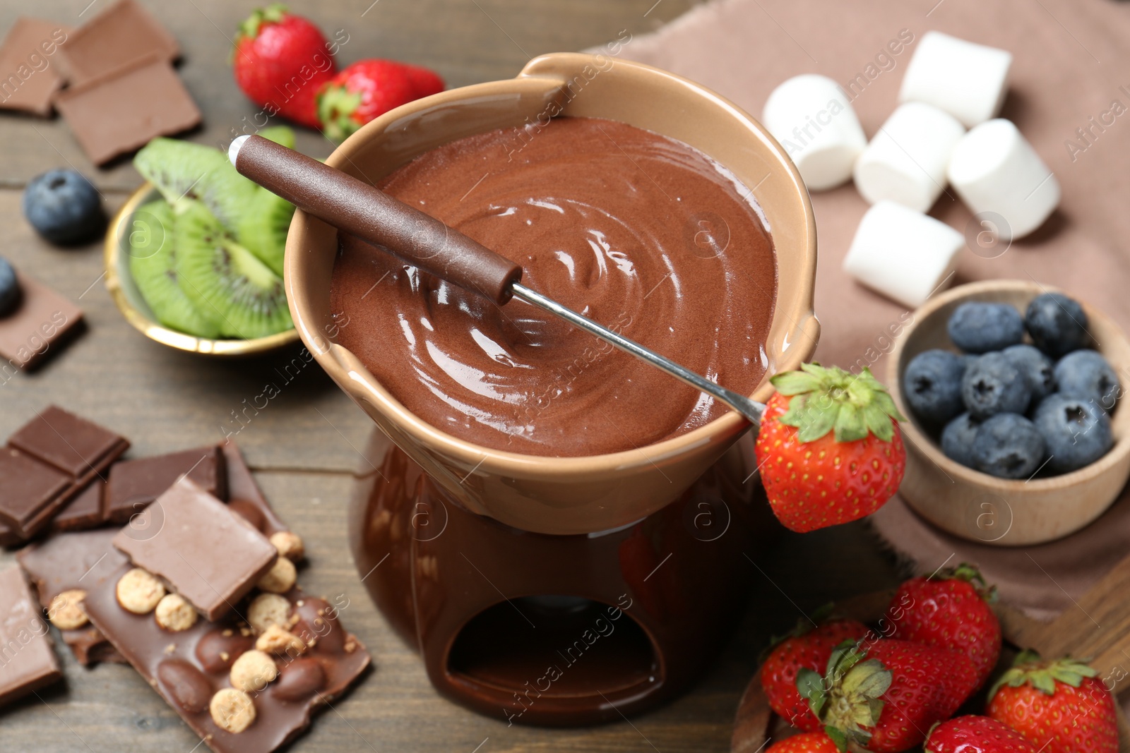 Photo of Fondue pot with melted chocolate, different fresh berries, kiwi and fork on wooden table