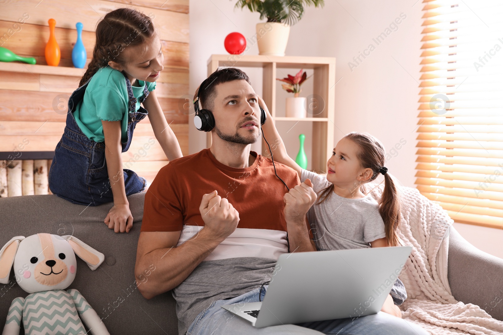 Photo of Children disturbing stressed man in living room. Working from home during quarantine