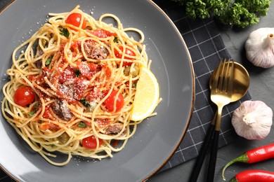 Photo of Plate of delicious pasta with anchovies, tomatoes and parmesan cheese near ingredients on black table, flat lay