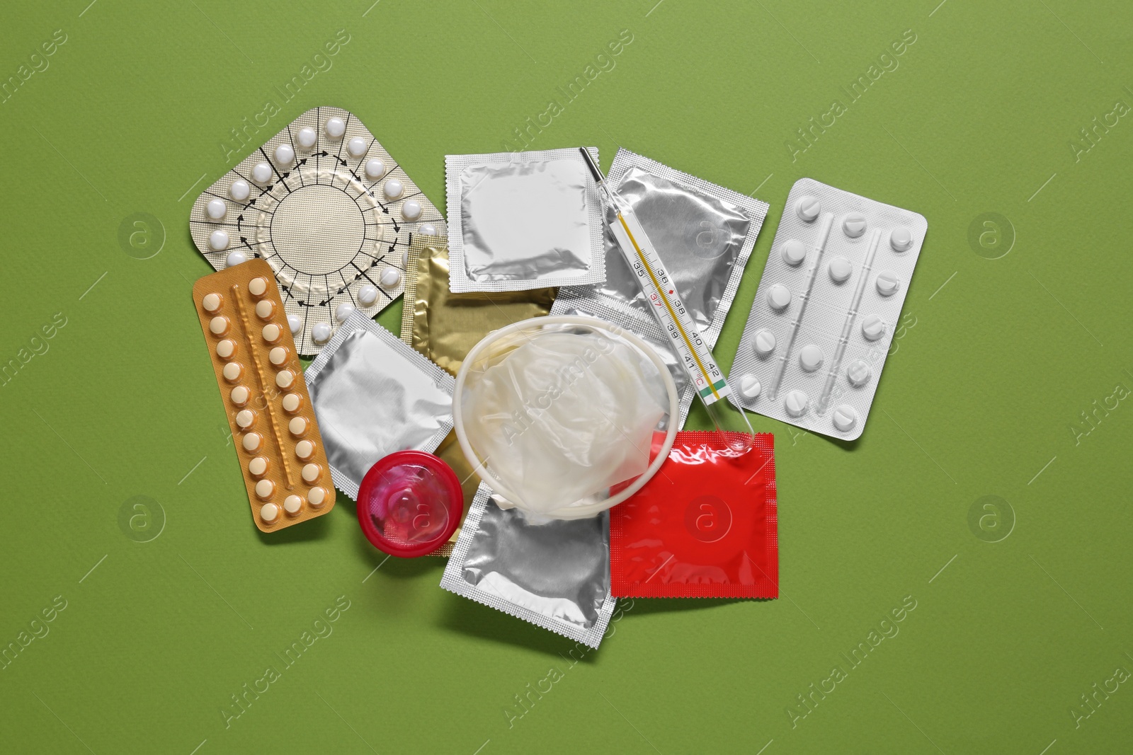 Photo of Contraceptive pills, condoms and thermometer on green background, flat lay. Different birth control methods