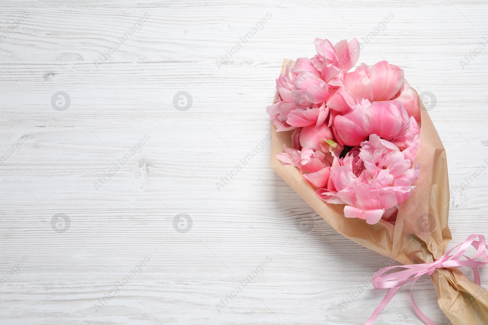 Photo of Beautiful bouquet of pink peonies wrapped in paper on white wooden table, top view. Space for text