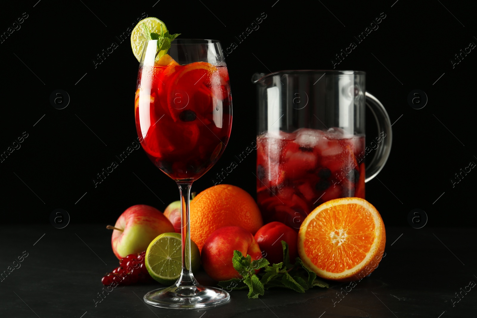 Photo of Glass and jug of Red Sangria with fruits on black table