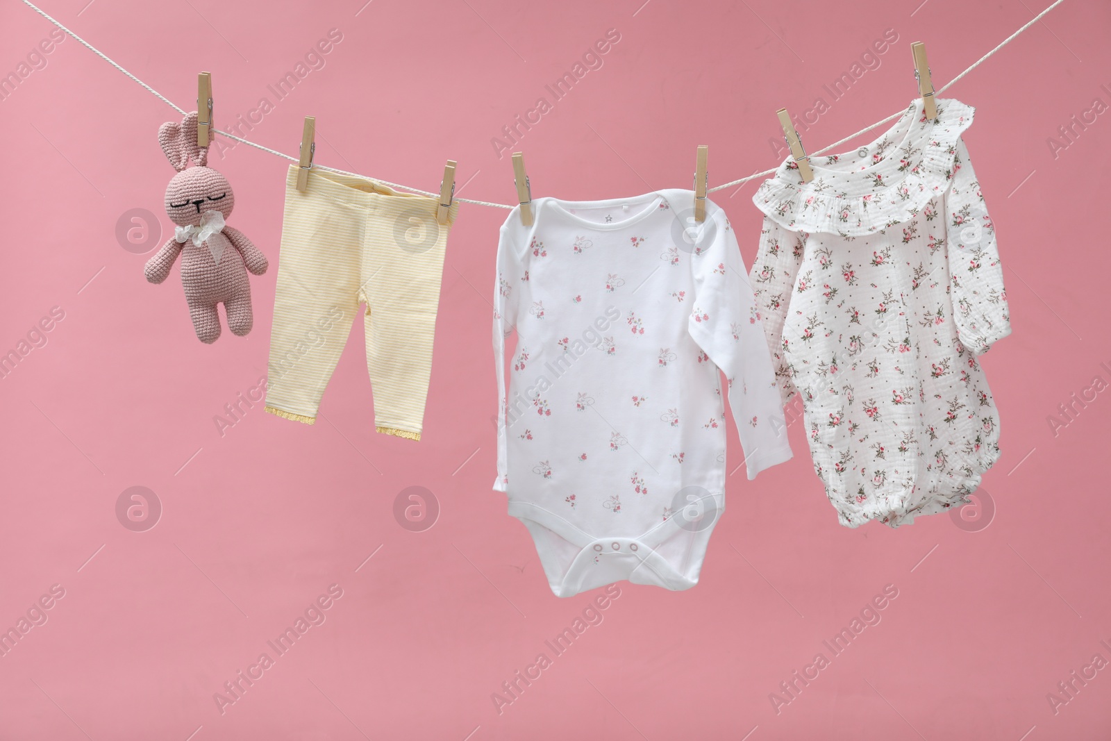 Photo of Different baby clothes and bunny toy drying on laundry line against pink background