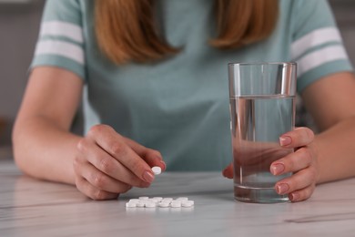 Photo of Woman with antidepressant pills and glass of water at table, closeup