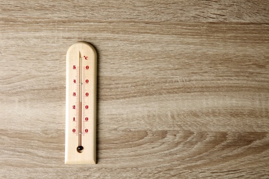 Photo of Weather thermometer on wooden table, top view. Space for text