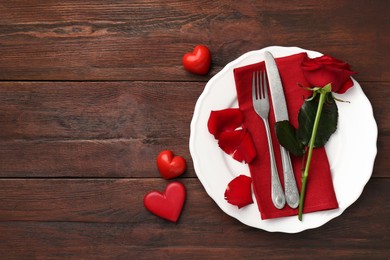 Photo of St. Valentine's day dinner. Romantic place setting with red rose and decorative hearts on wooden table, top view. Space for text