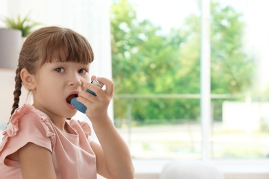 Photo of Little girl using asthma inhaler on blurred background