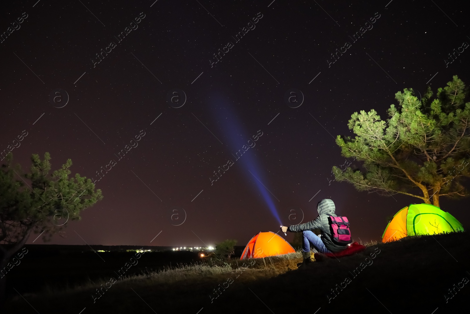 Photo of Man with bright flashlight near camping tents outdoors at night