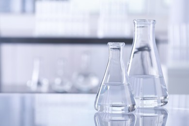 Photo of Conical flasks with transparent liquid on table in laboratory. Space for text