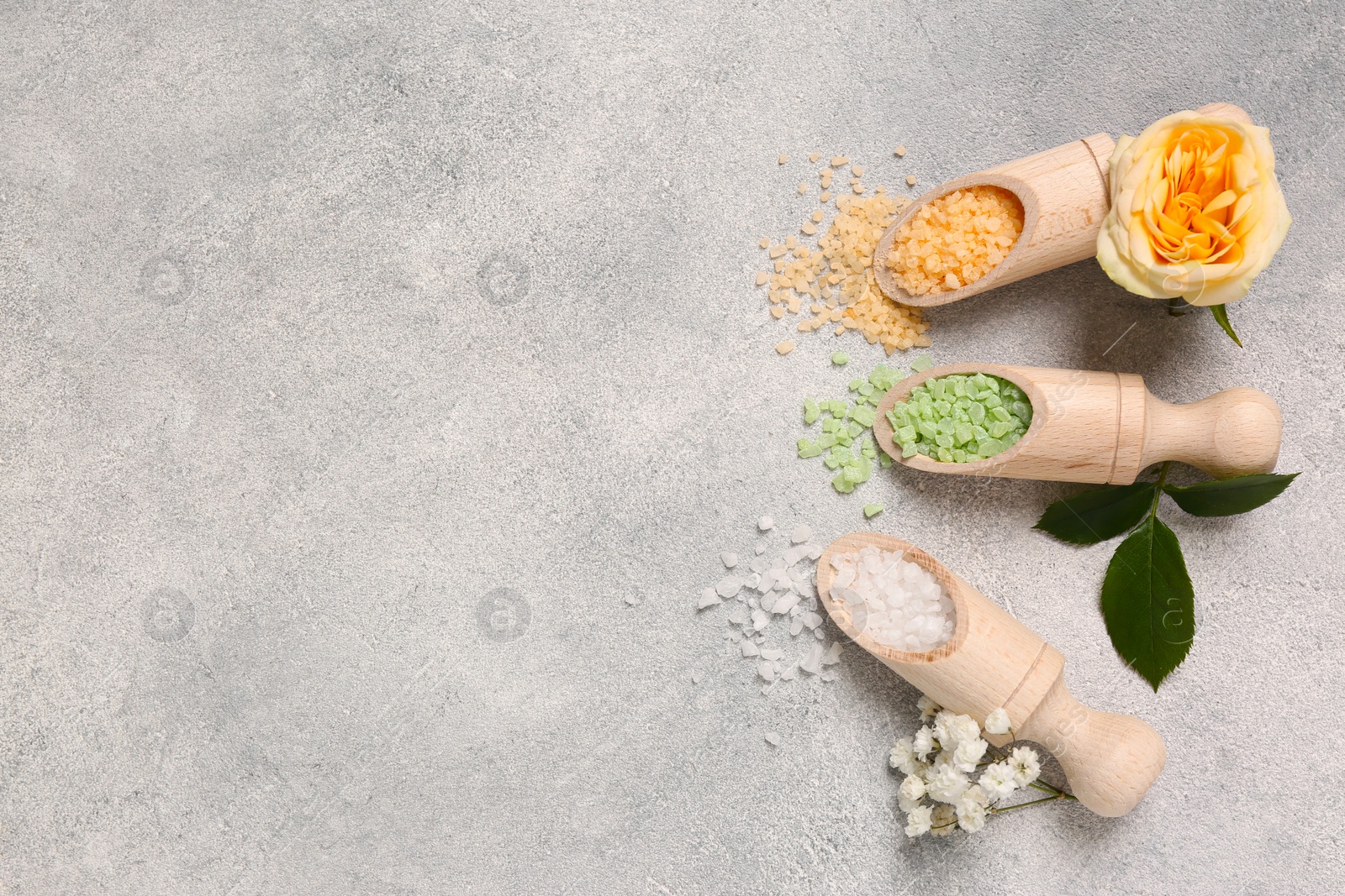 Photo of Scoops with different sea salt and flowers on light grey table, flat lay. Space for text