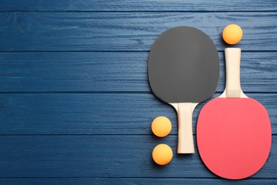 Photo of Ping pong rackets and balls on blue wooden table, flat lay. Space for text