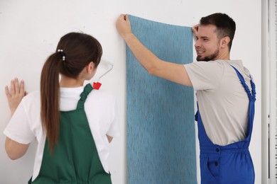 Photo of Workers hanging light blue wallpaper in room