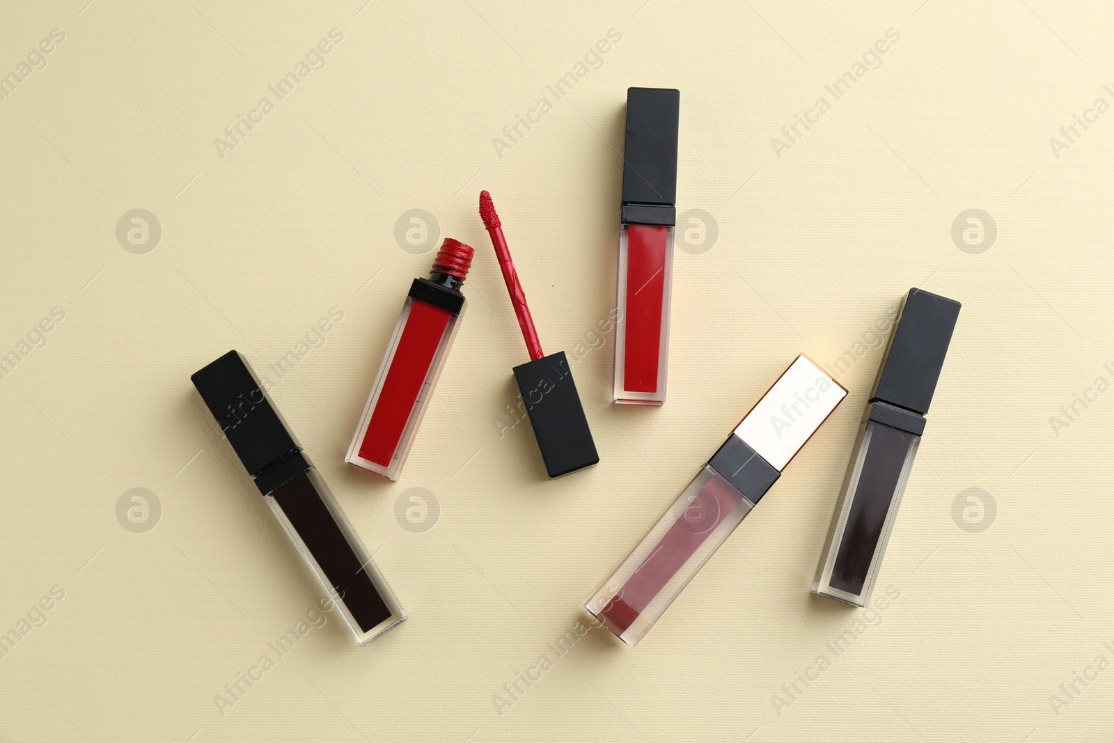 Photo of Different lip glosses and applicator on pale yellow background, flat lay