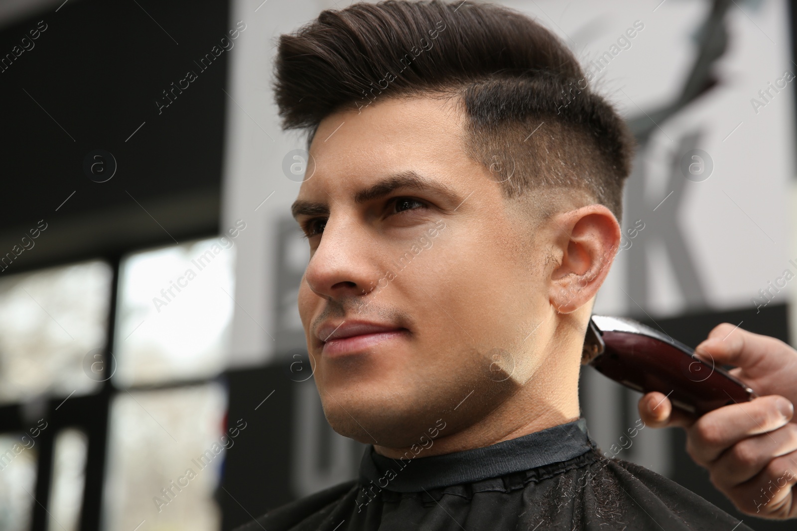 Photo of Professional barber making stylish haircut in salon, closeup