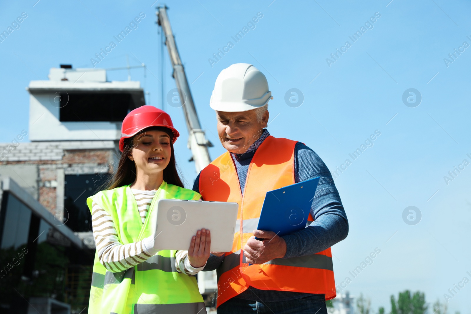 Photo of Professional engineer and foreman in safety equipment with tablet at construction site