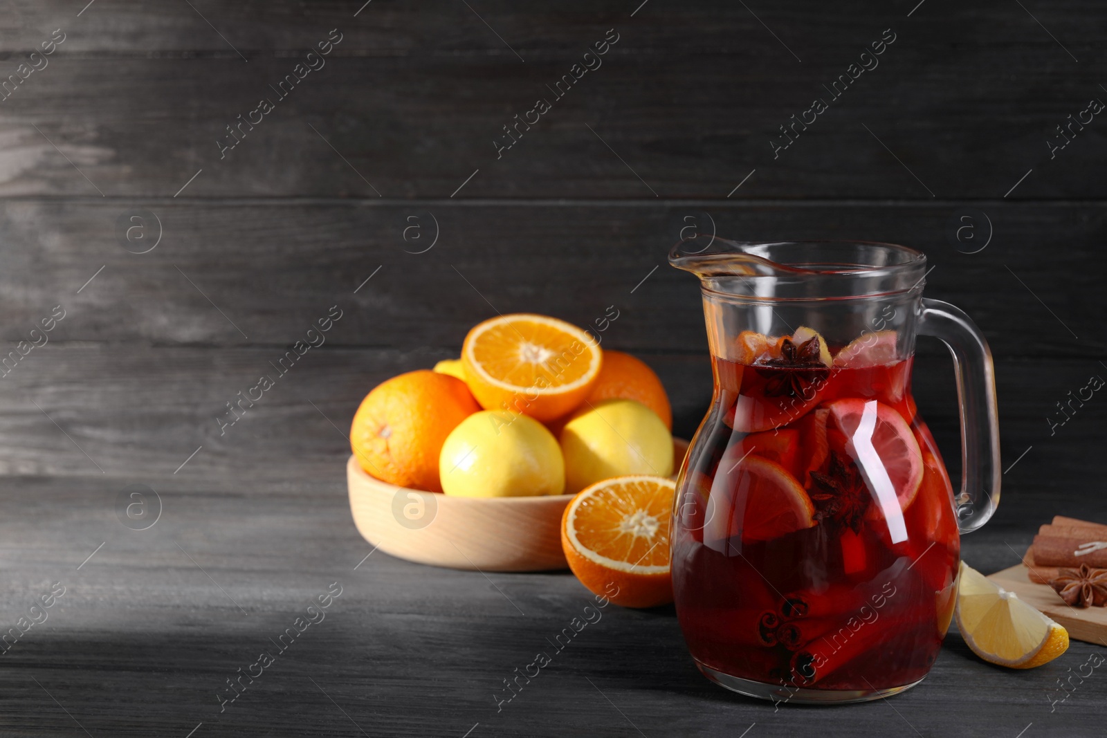 Photo of Glass jug of aromatic punch drink and ingredients on black wooden table. Space for text