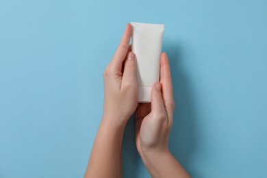 Woman with tube of hand cream on light blue background, top view