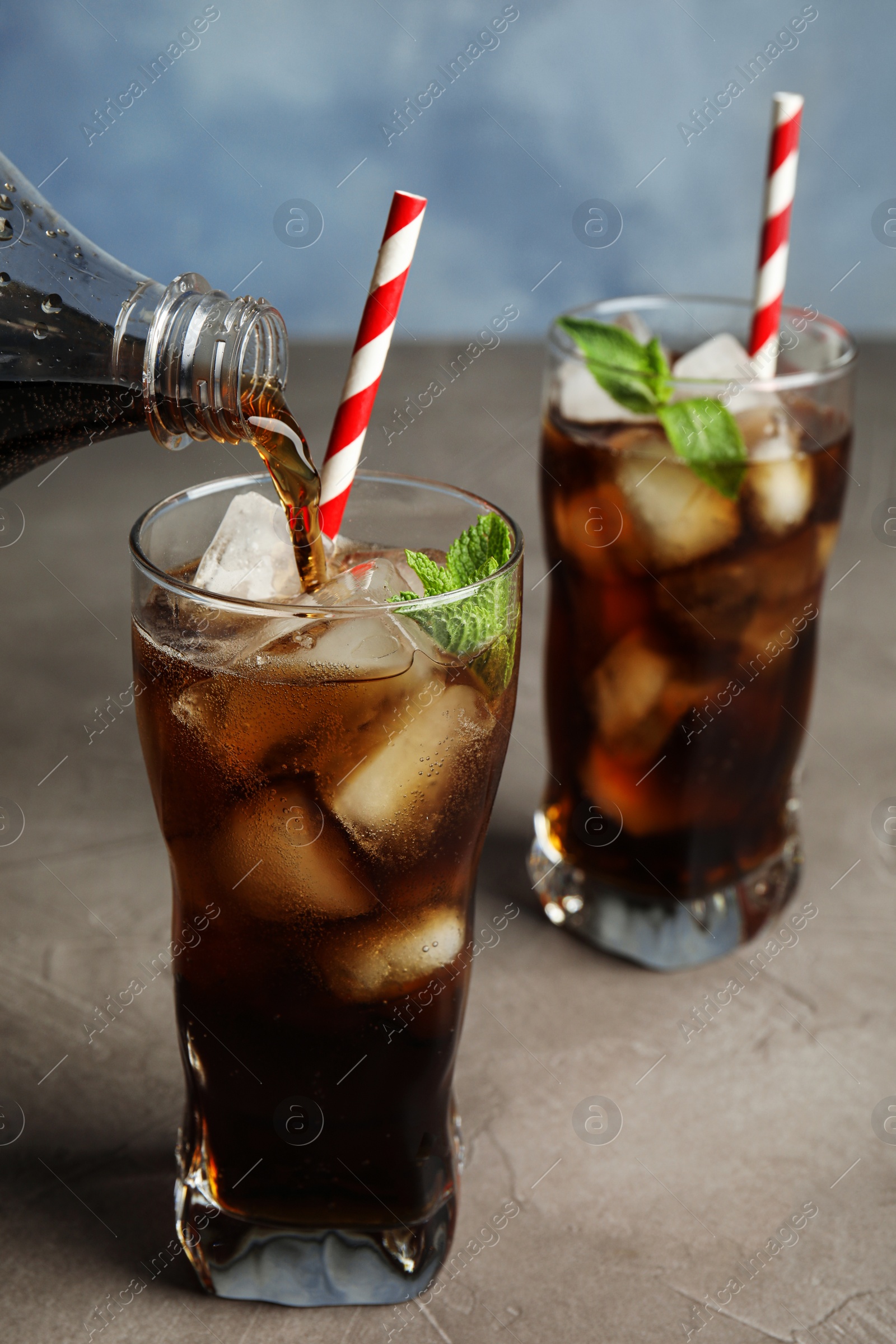 Photo of Pouring refreshing soda drink into glass on grey table against blue background