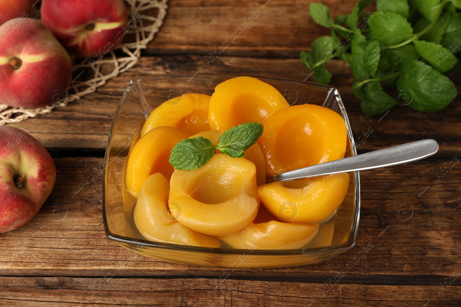 Photo of Canned peach halves in bowl on wooden table