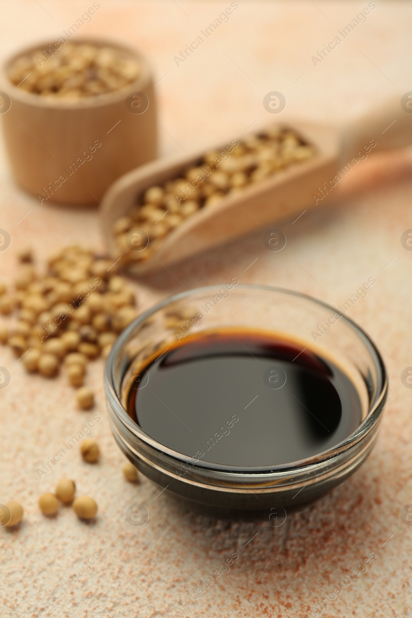 Photo of Soy sauce in bowl and beans on beige textured table, closeup