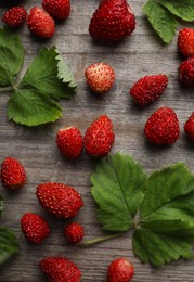 Many fresh wild strawberries and leaves on wooden table, flat lay