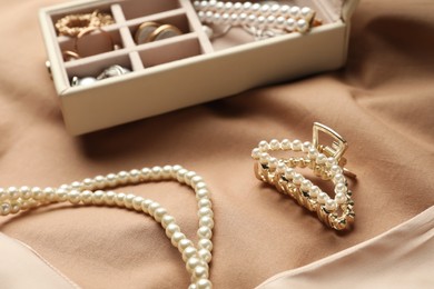 Photo of Elegant necklace, hair clip and box with luxurious pearl jewelry on beige fabric, closeup