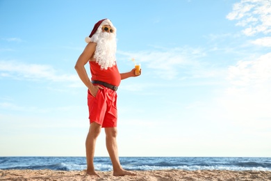 Photo of Santa Claus with cocktail on beach, space for text. Christmas vacation