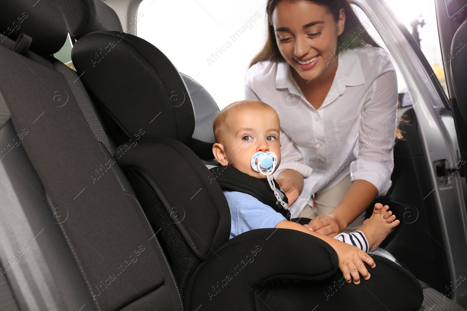 Photo of Mother fastening her son in child safety seat inside car