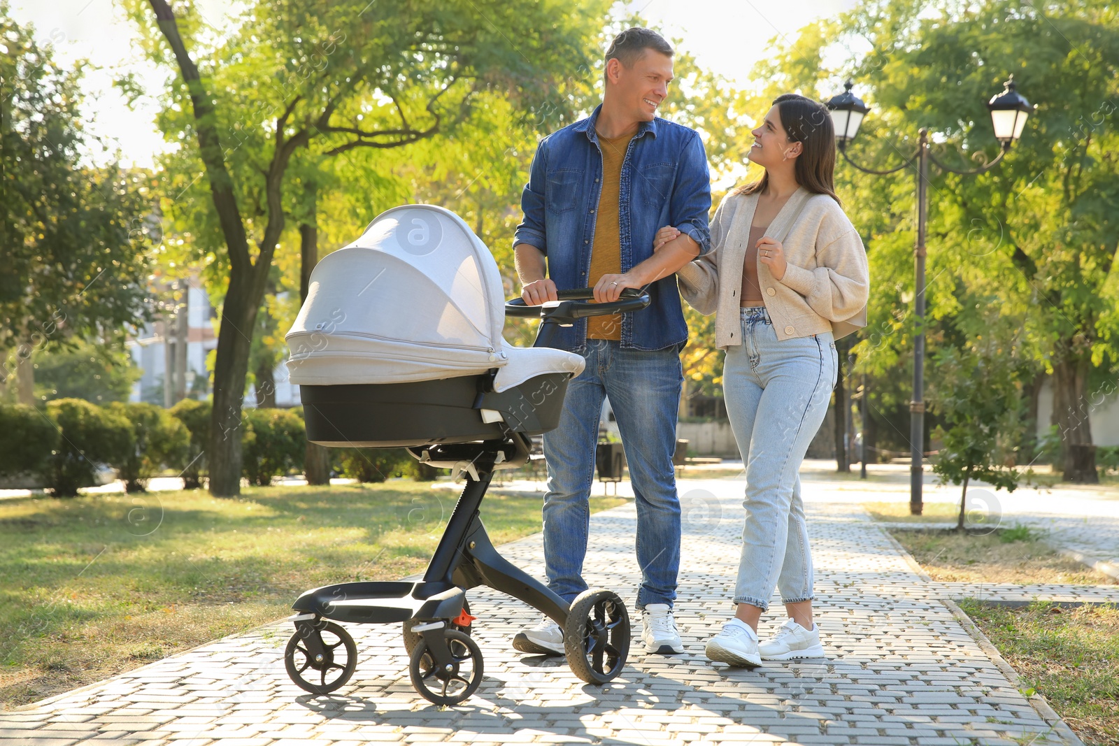 Photo of Happy parents walking with their baby in stroller at park on sunny day