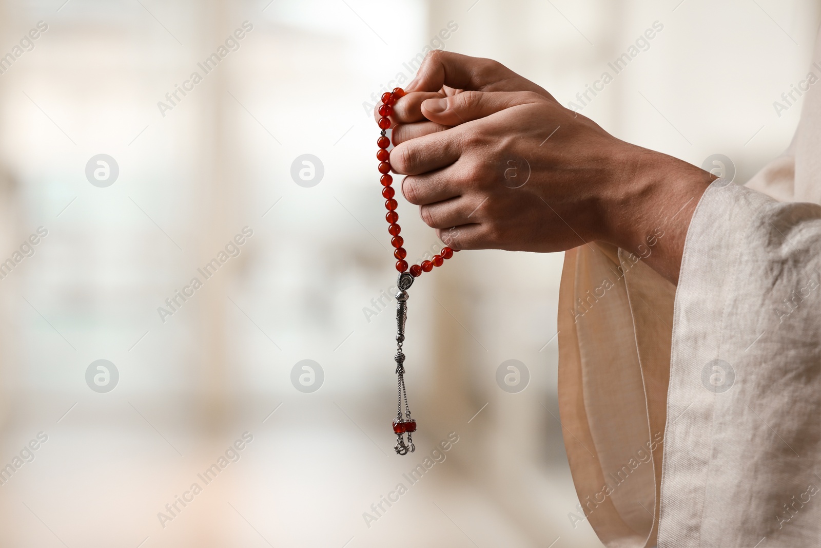 Image of Muslim man with misbaha praying on blurred background, closeup. Space for text