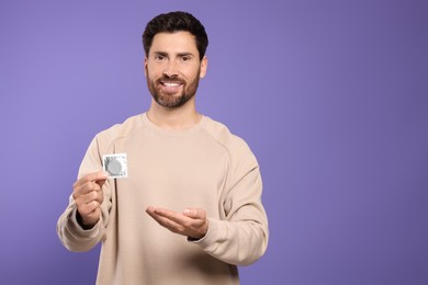 Man holding condom on purple background, space for text. Safe sex