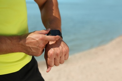 Young man checking pulse with smartwatch after training on beach, closeup. Space for text