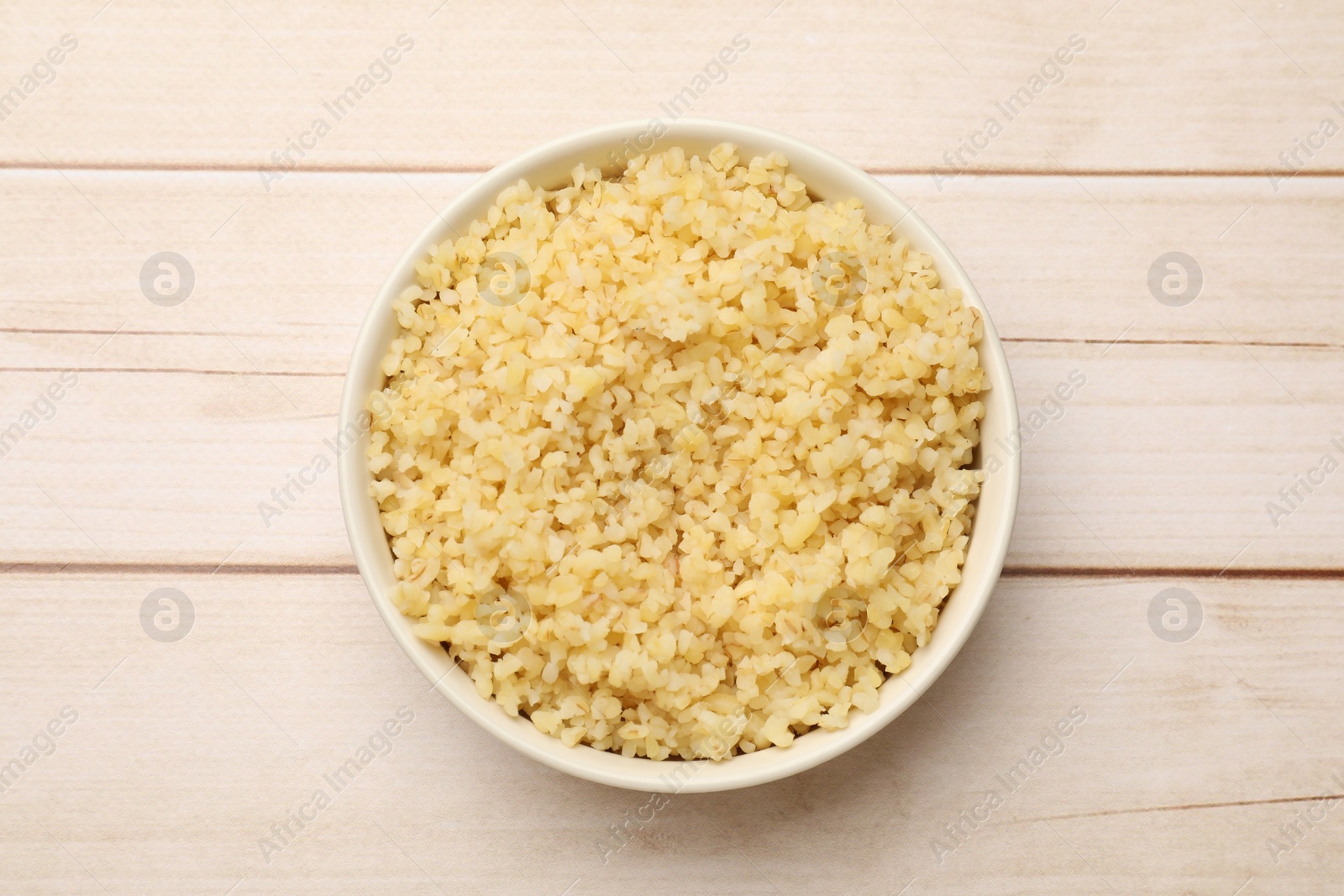 Photo of Delicious bulgur in bowl on wooden table, top view