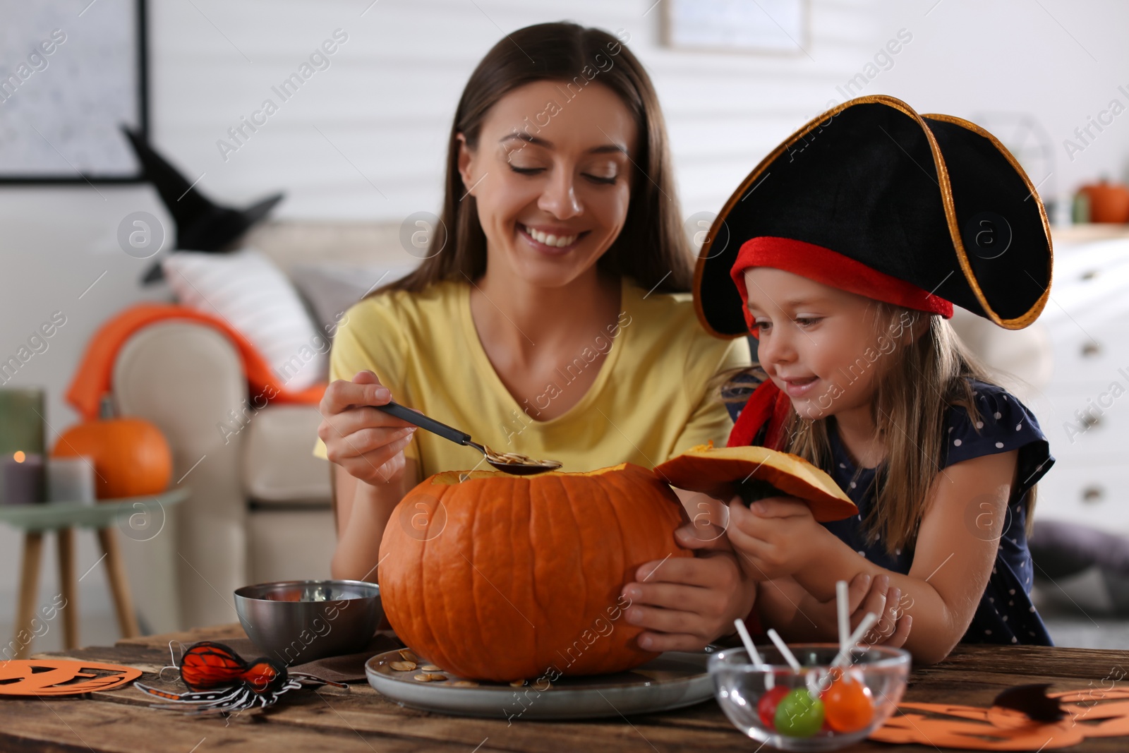 Photo of Mother and daughter making pumpkin jack o'lantern at table indoors. Halloween celebration