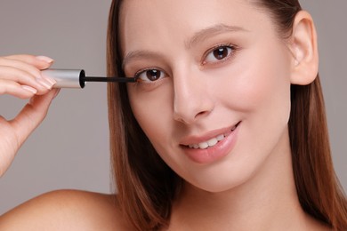 Photo of Beautiful woman applying serum onto eyelashes on grey background, closeup