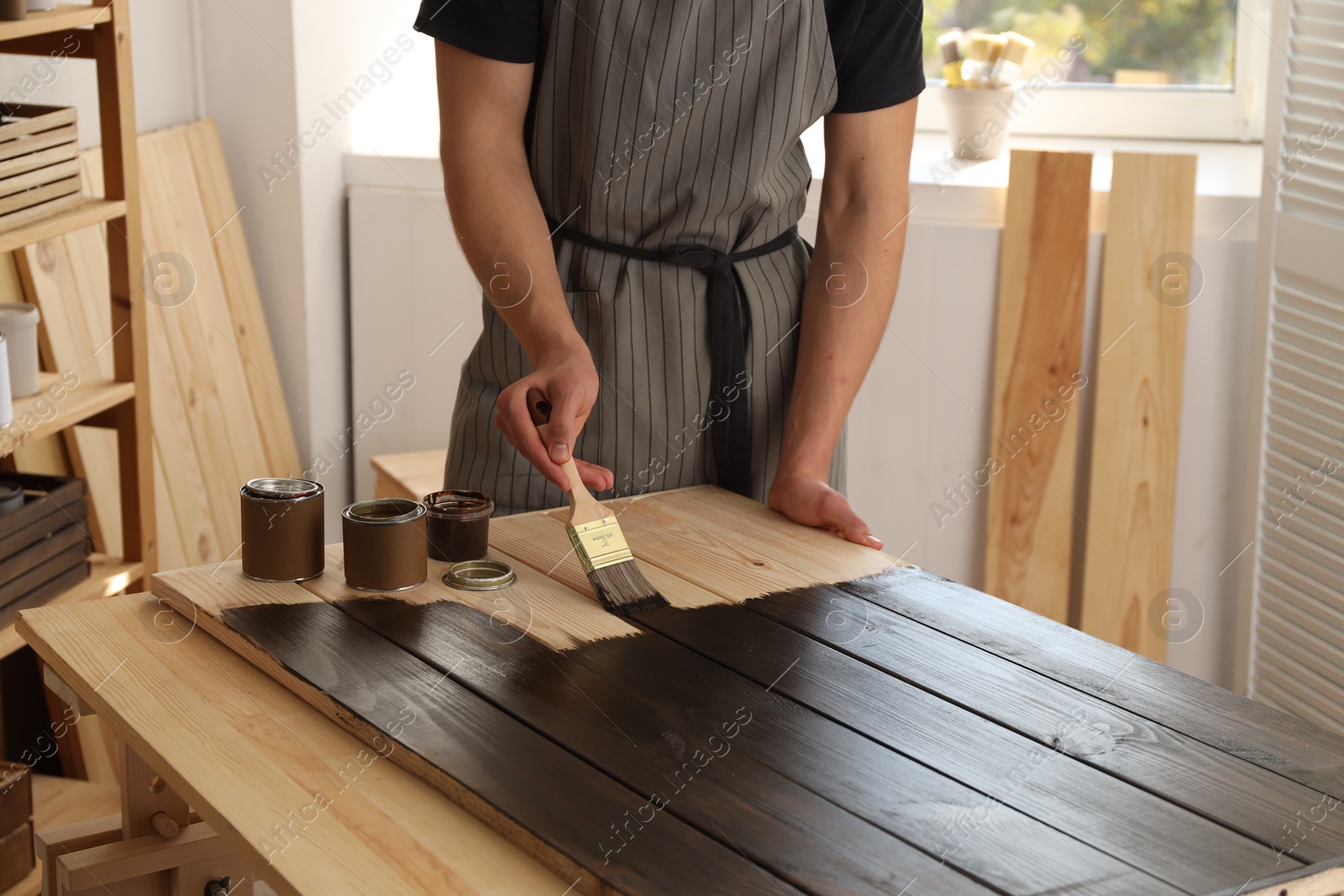 Photo of Man with brush applying wood stain onto wooden surface indoors, closeup