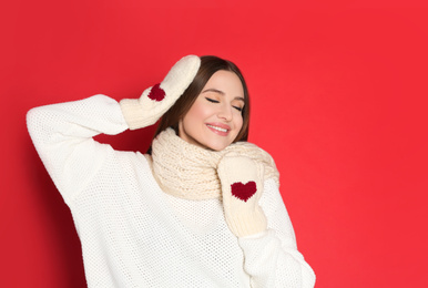 Young woman wearing warm sweater and mittens on red background. Winter season