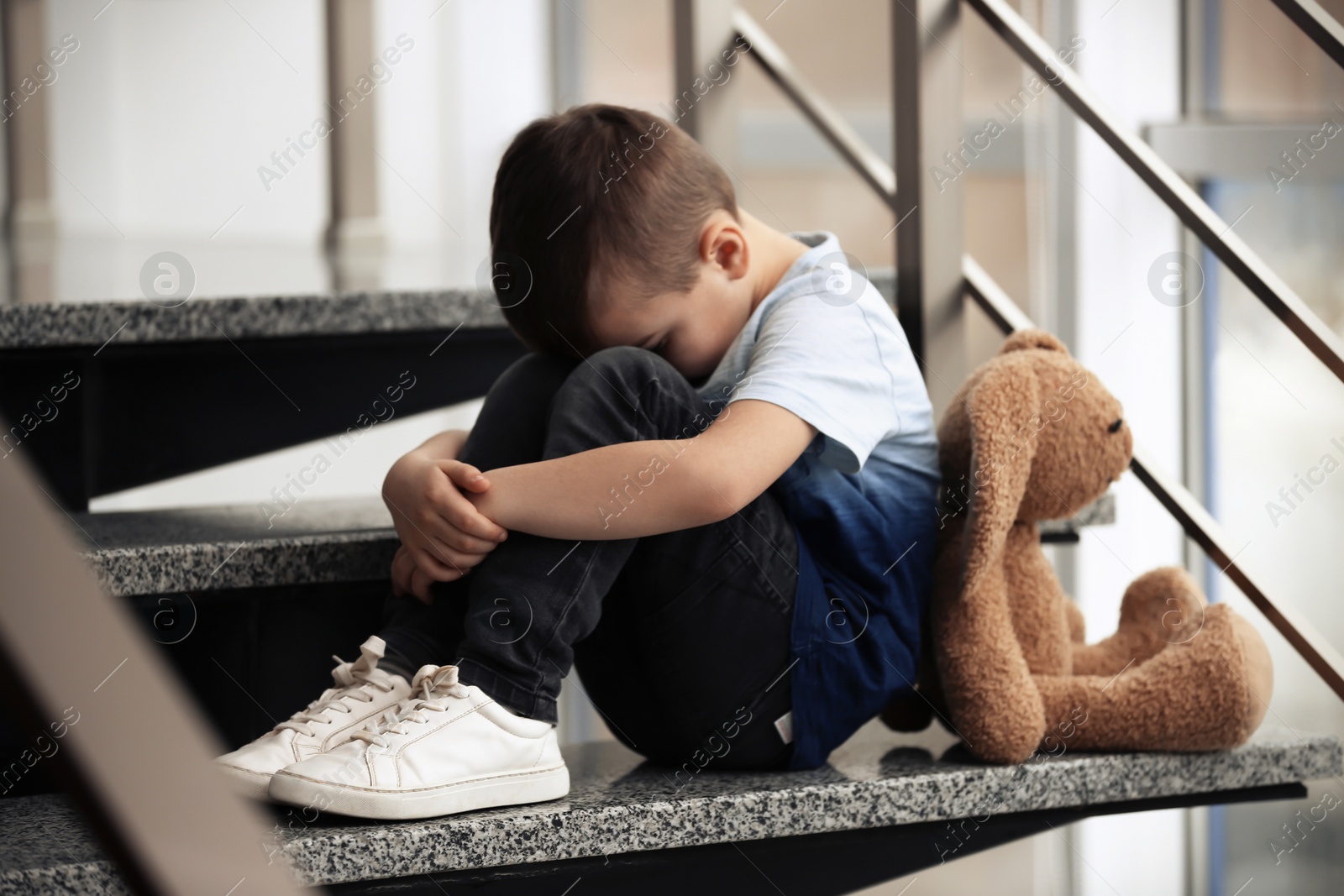 Photo of Sad little boy with toy sitting on stairs indoors