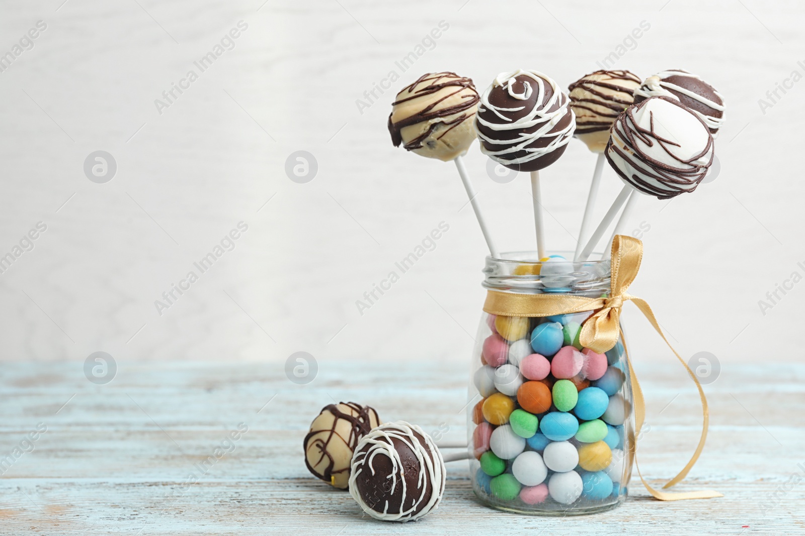 Photo of Glass jar with tasty cake pops and dragee on table against light background, space for text