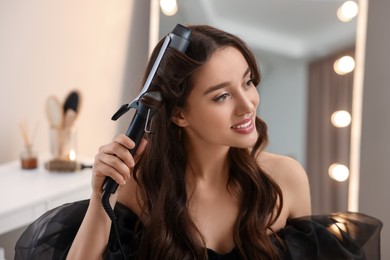 Photo of Smiling woman using curling hair iron at home