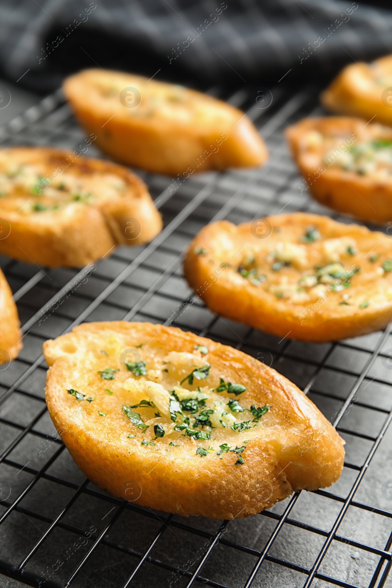 Photo of Baking rack with tasty homemade garlic bread on table, closeup